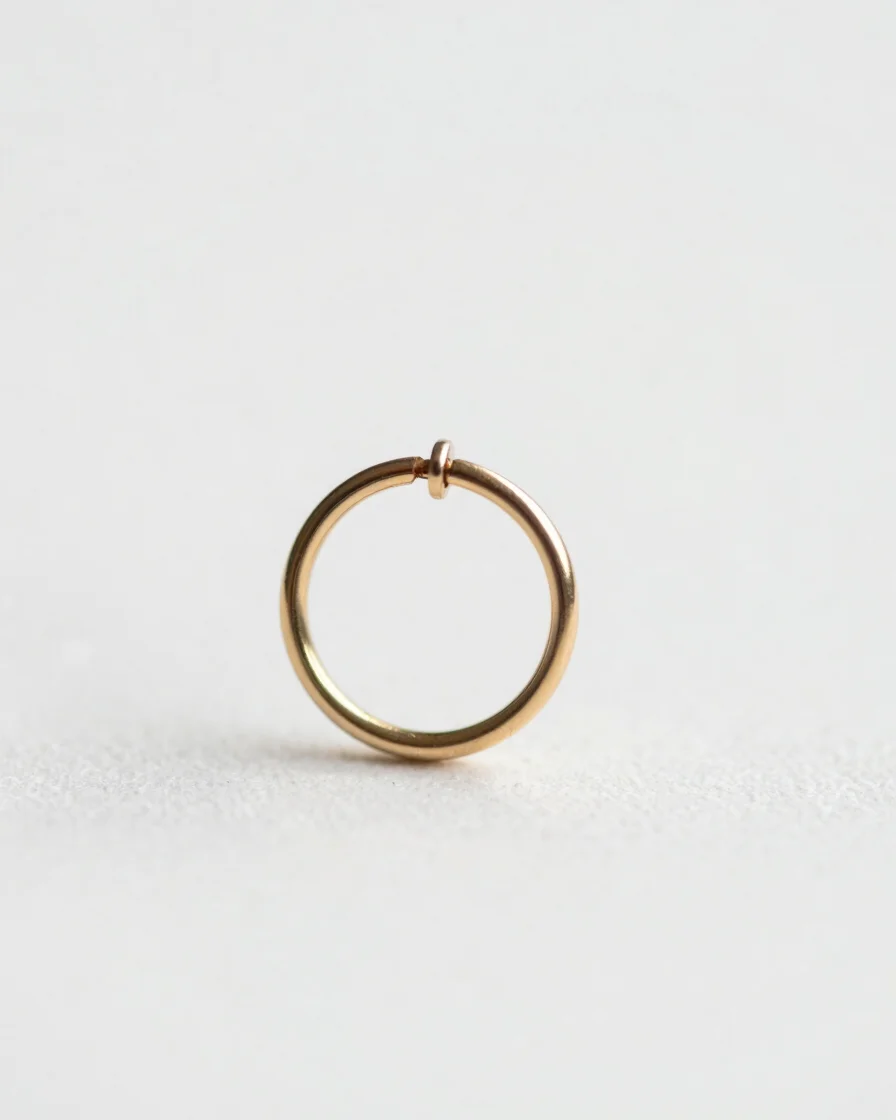 Macro close-up of a well-healed helix piercing with a delicate, minimalist gold hoop, soft daylight, clean white backgro